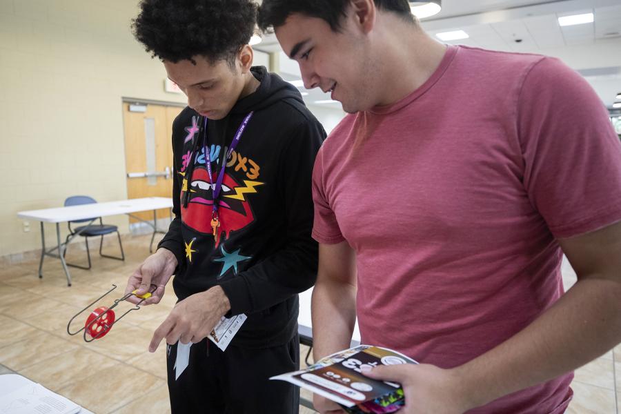 Two students look at a red device that uses magnets to regulate speed at the Engineering Club table.